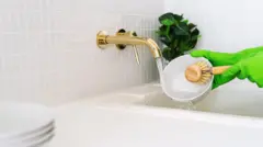 Foto de uma pessoa lavando uma cumbuca com uma escova de cozinha na pia.