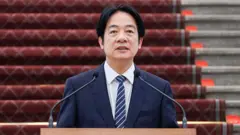 台灣總統賴清德身穿深藍色西裝，繫著條紋領帶，站在麥克風前。