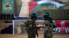 يقف مقاتلو حماس في تشكيل بينما يتجمع الفلسطينيون في أحد الشوارع لمشاهدة تسليم ثلاث رهائن إسرائيليين لفريق الصليب الأحمر في دير البلح، وسط غزة، في 8 فبراير 2025.