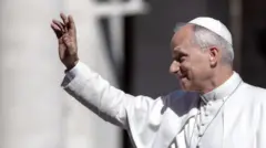 Papież – ubrany na biało – pozdrawia tłum z papamobilu ruchem lewej ręki. Mężczyźni lub chłopcy w mundurach robią sobie zdjęcia w tle.