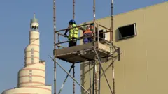 Dois trabalhadores em andaime, perto de construções
