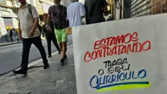Uma placa em frente a uma loja no centro de São Paulo onde se lê: "Estamos contratando, traga o seu currículo"
