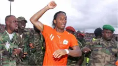 Drogba is escorted from the Bouake pitch by security personnel