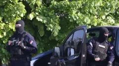 Policajci sa pokrivenim licima stoje napolju, ispred vozila, iza je zelenilo