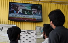 Televizyonda Hamaney ve Trump'ın fotoğrafları var. Üç kişi arkadan çekilen fotoğraflarında televizyondaki haberleri izliyor