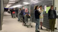Shoppers wait to enter a supermarket in the suburb of Johnsonville in Wellington