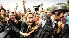 Uighur women grab a riot policemen as they protest in Urumqi in China's far west Xinjiang province on July 7, 2009