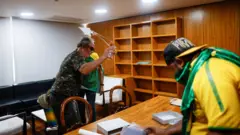 Homens com roupas militares e camisetas do Brasil vandalizam sala do planalto