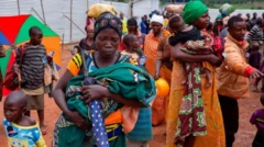 Ifoto irimwo abana, abagore bapfunze ibitambara mu mutwe, bateruye abana, umwe muri aba bana afise umutaka, harimwo n'umugabo ashaka gukora ku mutwe w'umwana