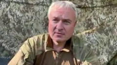 Седой мужчина в камуфляжной форме на фоне маскировочной сетки