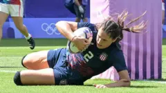 Ilona Maher, jogadora de rugby dos Estados Unidos, segura a bola deitada no chão em partida durante os Jogos Olímpicos de 2024, em Paris, na França
