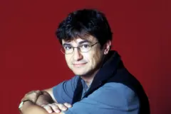 Carlo Rovelli com uma camisa azul sobre fundo vermelho