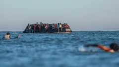 Gente nadando para intentar subir a un bote para migrantes hacia el Canal de la Mancha.