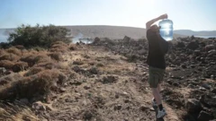 مردی در حال حمل بطری بزرگ آب روی شانه در یک راه خاکی