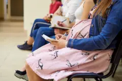 Mulheres grávidas sentadas em uma sala de espera segurando um bloco de notas e caneta