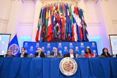 Vista de uma reunião da OEA, mostrando as bandeiras de seus membros e o símbolo da organização.