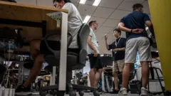 Cuatro hombres en pantalones cortos en una oficina en Tokio, Japón. Tres de ellos de pie, uno sentado con los codos apoyados en la mesa.