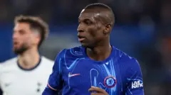 Nicolas Jackson, vêtu d'un maillot bleu de Chelsea, regarde vers sa droite lors d'un match contre Tottenham, tandis qu'un joueur de l'équipe adverse est flou à l'arrière-plan.