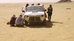 በክፍት መኪና በሱዳን በረሃ የሚጓዙ ሰዎች