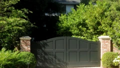 Casa vista de frente, com portão alto e arbustos