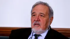 İlber Ortaylı ceketli ve kravatlı oturuyor konuşuyor.