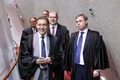 Kassio Nunes caminha no corredor para o plenário do TSE, seguido de André Mendonça e Dias Toffoli, todos de terno e toga.
