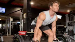 Dr Michael lifting weights at the gym in a grey singlet
