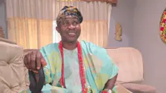 Wale Akorede Okunnu wọ agbada pẹlu fila, o tun mu ọpa lọwọ