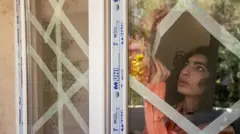 زنی برای جلوگیری از خرد شدن شیشه پنجرهها بر اثر موج حملات هوایی به پنجرهها چسب میزند