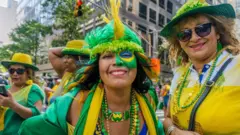 Duas brasileiras durante o evento Brazilian Day em Nova York, em 2016. Elas vestem roupas verdes e amarelas e uma delas tem o rosto parcialmente pintado com a bandeira brasileira