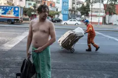 Un hombre en toalla en la mitad de la calle mientras detrás pasa un recogedor de cartón.