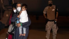 Two Afghan women with a child walk past a Spanish soldier after disembarking from an airplane