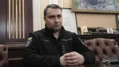 Кирило Буданов у чорній кофті сидить на шкіряному дивані в кабінеті, склавши руки на столі