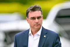 Flávio Bolsonaro olhando para o lado. Ele está de terno e usa óculos