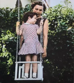 Alina Fernández de pé sobre um balanço com sua mãe atrás dela, em dia de sol
