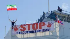 Protesters hold a banner saying "stop executions in Iran" and wave an Iranian flag during a demonstration on the roof of the Trocadero, overlooking Piccadilly Circus, central London (30 July 2026)