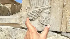 Una mano muestra el perfil de un rostro esculpido en una pared de piedra