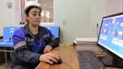 Ишлаб чиқариш корхонасида каска кийган ва компютерни бошқараётган ўзбек аёли