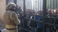 A fighter in military uniform looks at men on the other side of a metal gate in Damascus 