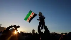 حشود سورية تحتفل بسقوط حكم الأسد حيث يظهر في الصورة طفل يحمل على سوريا الذي تبناه معارضو الأسد