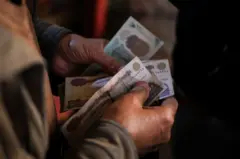 مبلغ من النقود في يد رجل، صورة بتاريخ فبراير ٢٠٢٥