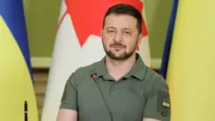 الرئيس الأوكراني فولوديمير زيلينسكي أمام علم أوكرانيا وكندا