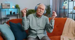 Homem idoso respira profundamente, com gesto de mudra e olhos fechados, meditando com a mente concentrada e serena em casa