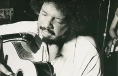 Tim Maia cantando com os olhos fechados e tocando violão