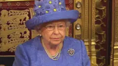 Rainha Elizabeth usando uma roupa e chapéu azul e colar de pérolas
