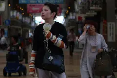 Una mujer en Japón con un ventilador portátil, mientras otra detrás se seca el sudor de la frente con un pañuelo.