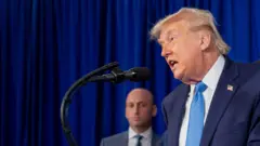 Trump habla frente a un micrófono. En el fondo, se ve al asesor de Seguridad Nacional, Stephen Miller.