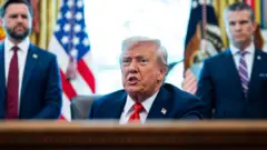 O vice-presidente dos EUA, JD Vance (à esquerda), o presidente Donald Trump e o secretário de Defesa dos EUA, Pete Hegseth, durante a assinatura de um decreto no Salão Oval da Casa Branca, em Washington D.C.