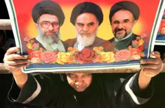 Seorang perempuan Iran memegang poster pemimpin tertinggi Iran Ayatollah Ali Khamenei (kiri), pendahulunya mendiang Ayatollah Ruhollah Khomeini dan Presiden Iran (saat itu) Mohammad Khatami, dalam rapat umum 23 Mei 2000.