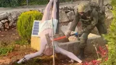 Израильский солдат ударяет кувалдой по голове перевернутой статуи Иисуса Христа на юге Ливана. Фото: апрель 2026 г.